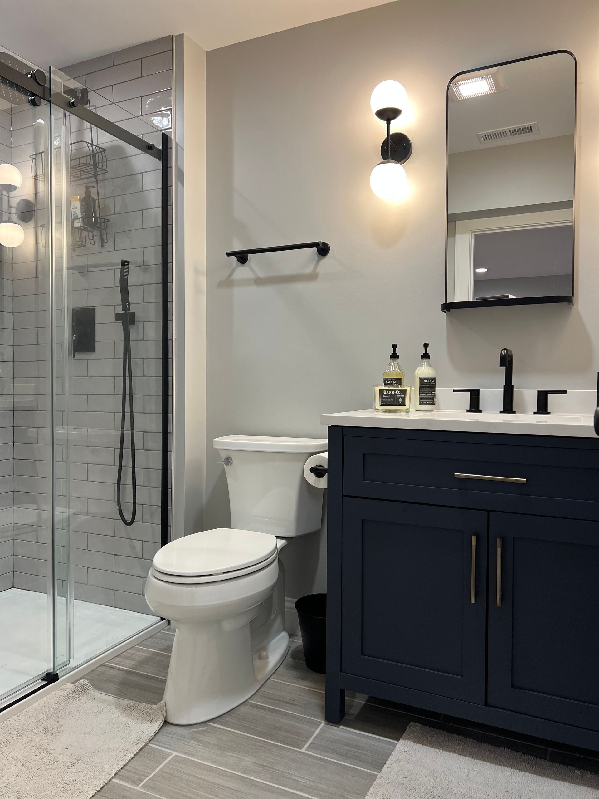 Modern bathroom with blue vanity, black fixtures, and glass shower.