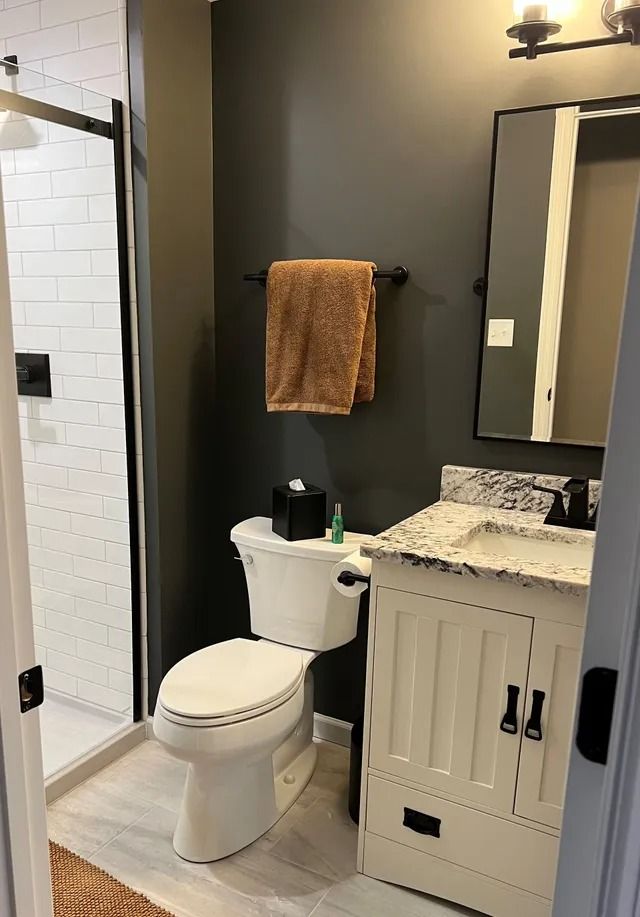 Bathroom with gray walls, white toilet, vanity, and shower. Tan towel and black fixtures.