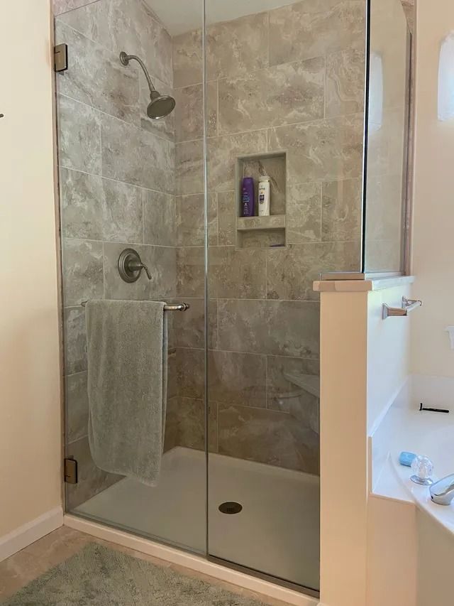 Glass shower with gray tile, shower head, and towel bar; white shower base.