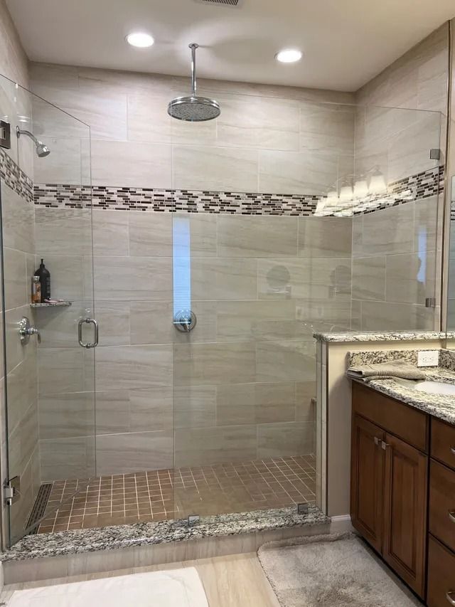 Walk-in shower with glass doors, tiled walls/floor, overhead showerhead, and vanity on the right.