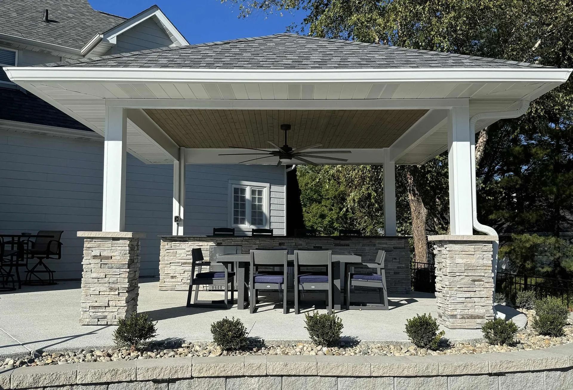 Outdoor covered patio with stone pillars, dining table, and ceiling fan.