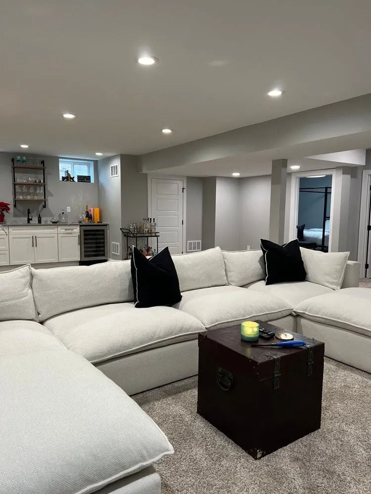 Cozy basement living area with a large white sectional sofa, a dark wooden trunk coffee table, and a small bar area.