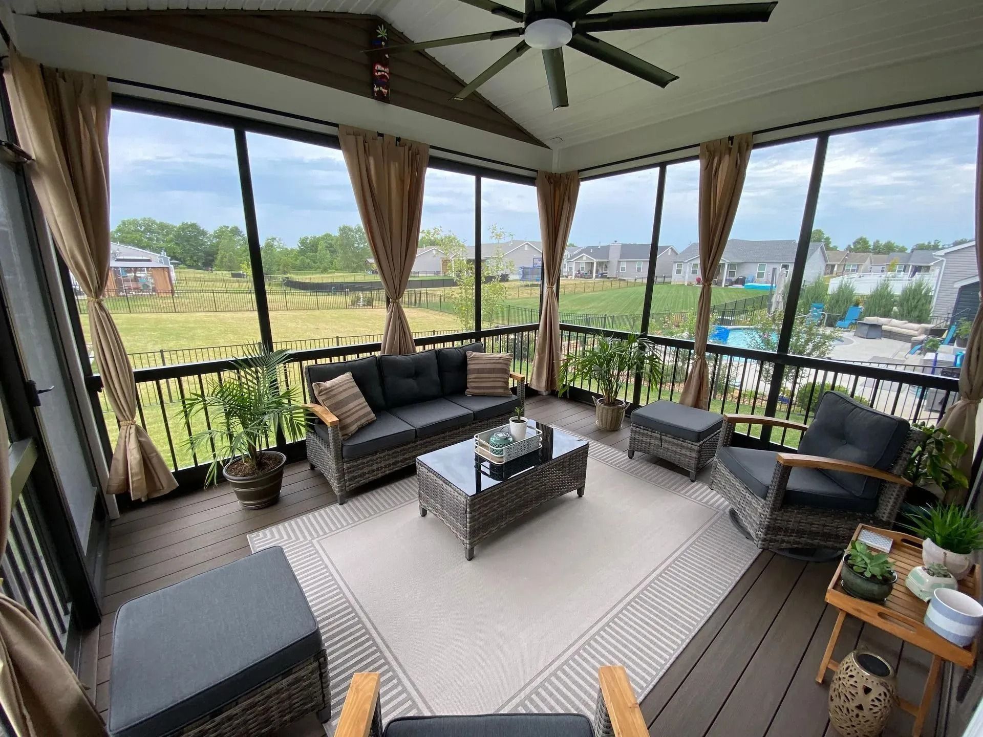 Screened porch with gray wicker furniture, beige curtains, and a view of a field.