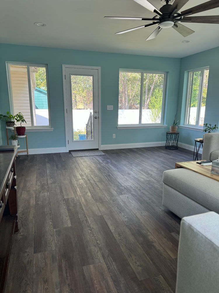 Living room with turquoise walls, dark wood-look flooring, large windows, and a ceiling fan.