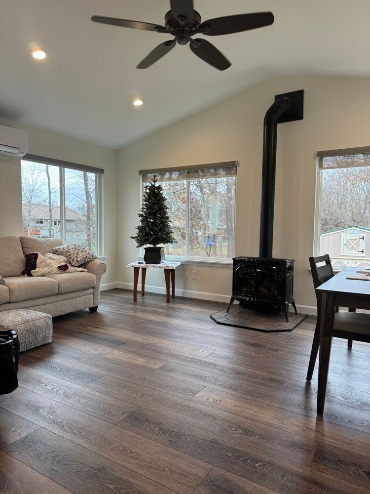 Living room with dark wood floors, couch, wood stove, and ceiling fan.