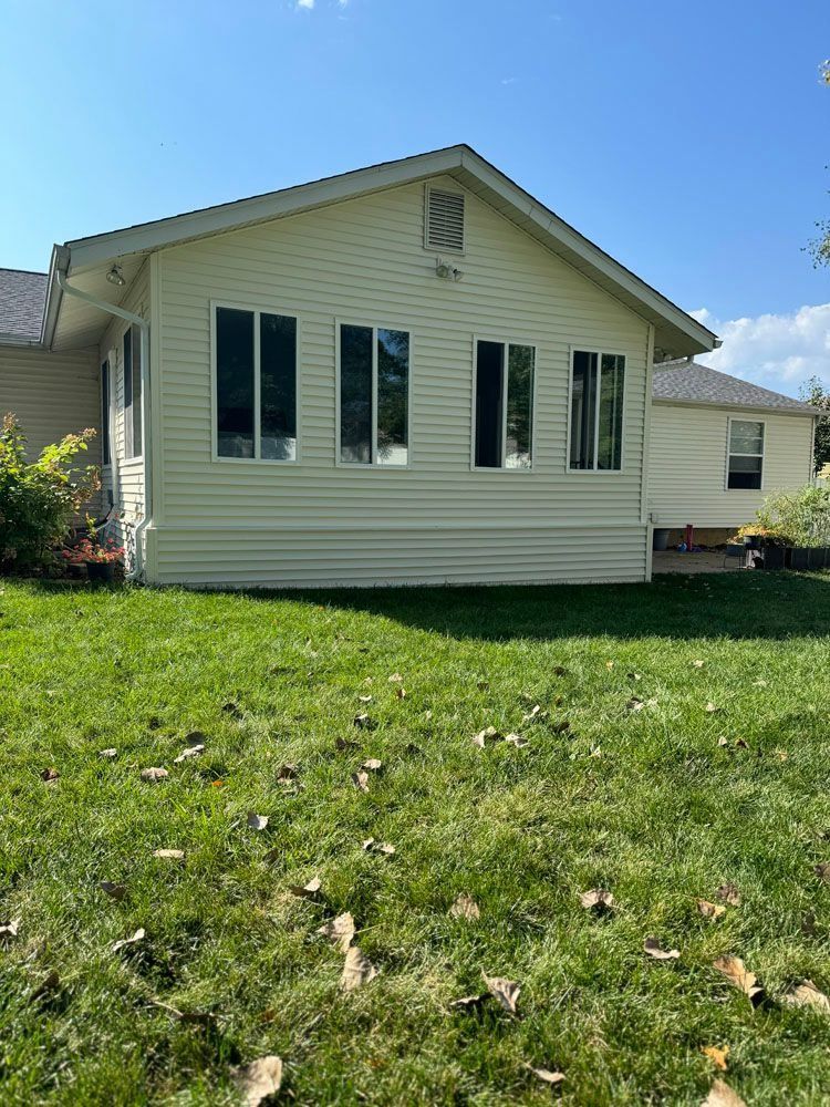 A light yellow house extension with three tall windows, set on a green lawn against a blue sky.