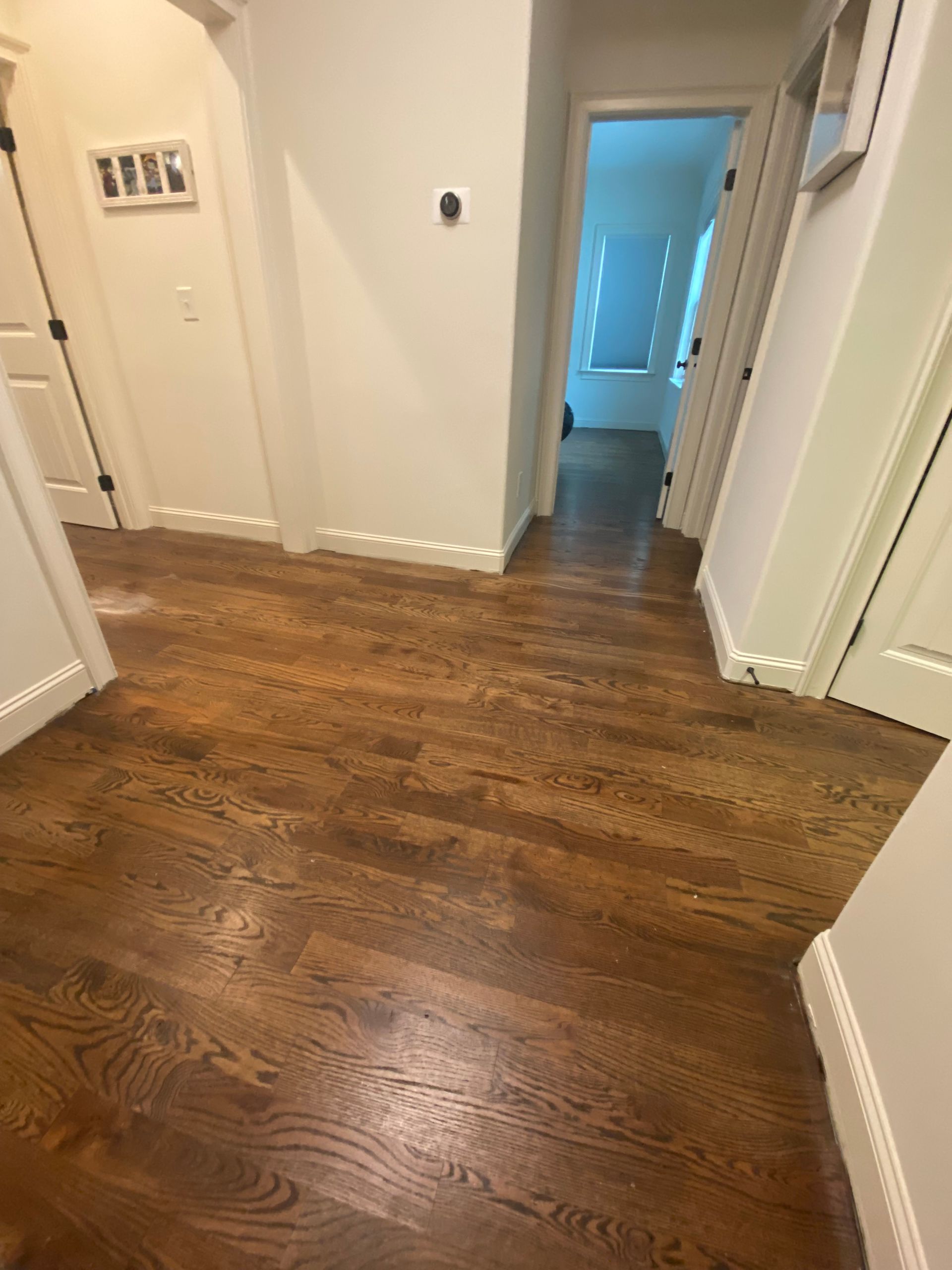 Wooden hallway with white walls, doorways, and a glimpse of sunlight.