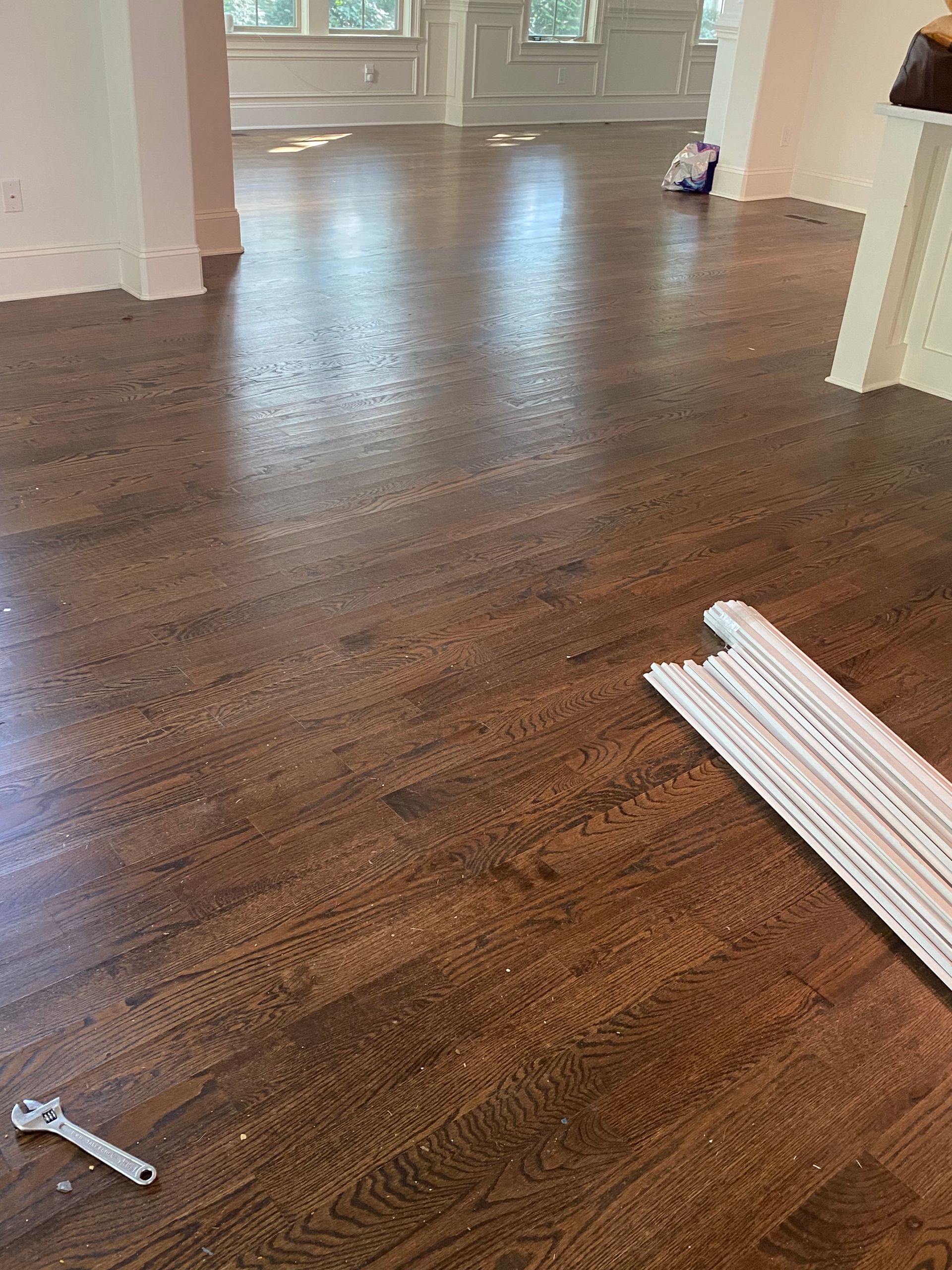 Dark stained hardwood floor with debris, trim pieces, and a wrench scattered.