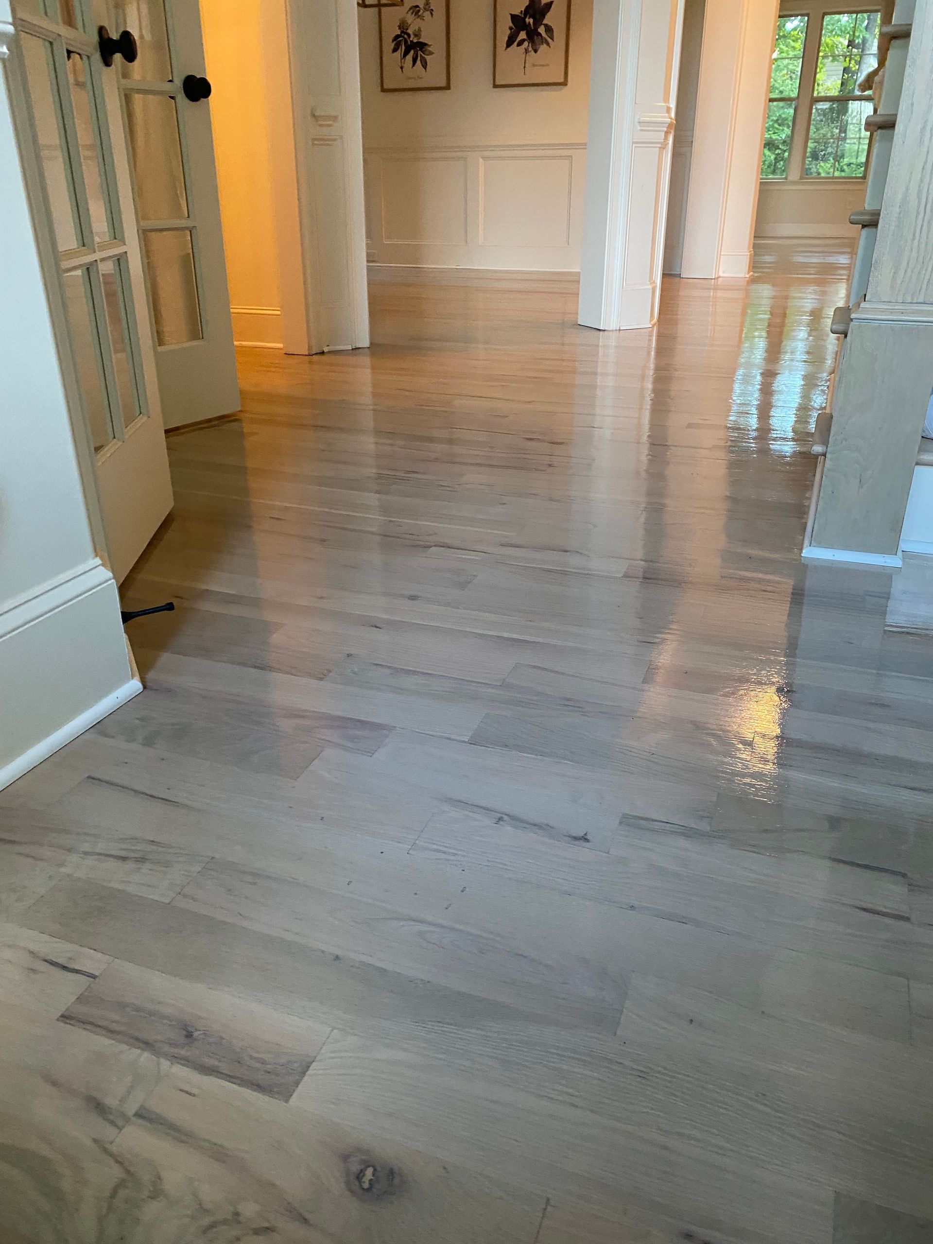 Shiny, light-colored hardwood floors in a hallway, reflecting light. White pillars and doorways are visible.