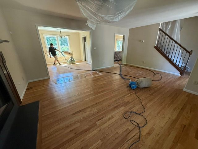 A man is cleaning a wooden floor in a living room with a vacuum cleaner.
