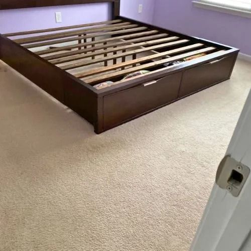 A bed frame with drawers underneath it is sitting on a carpeted floor in a bedroom.