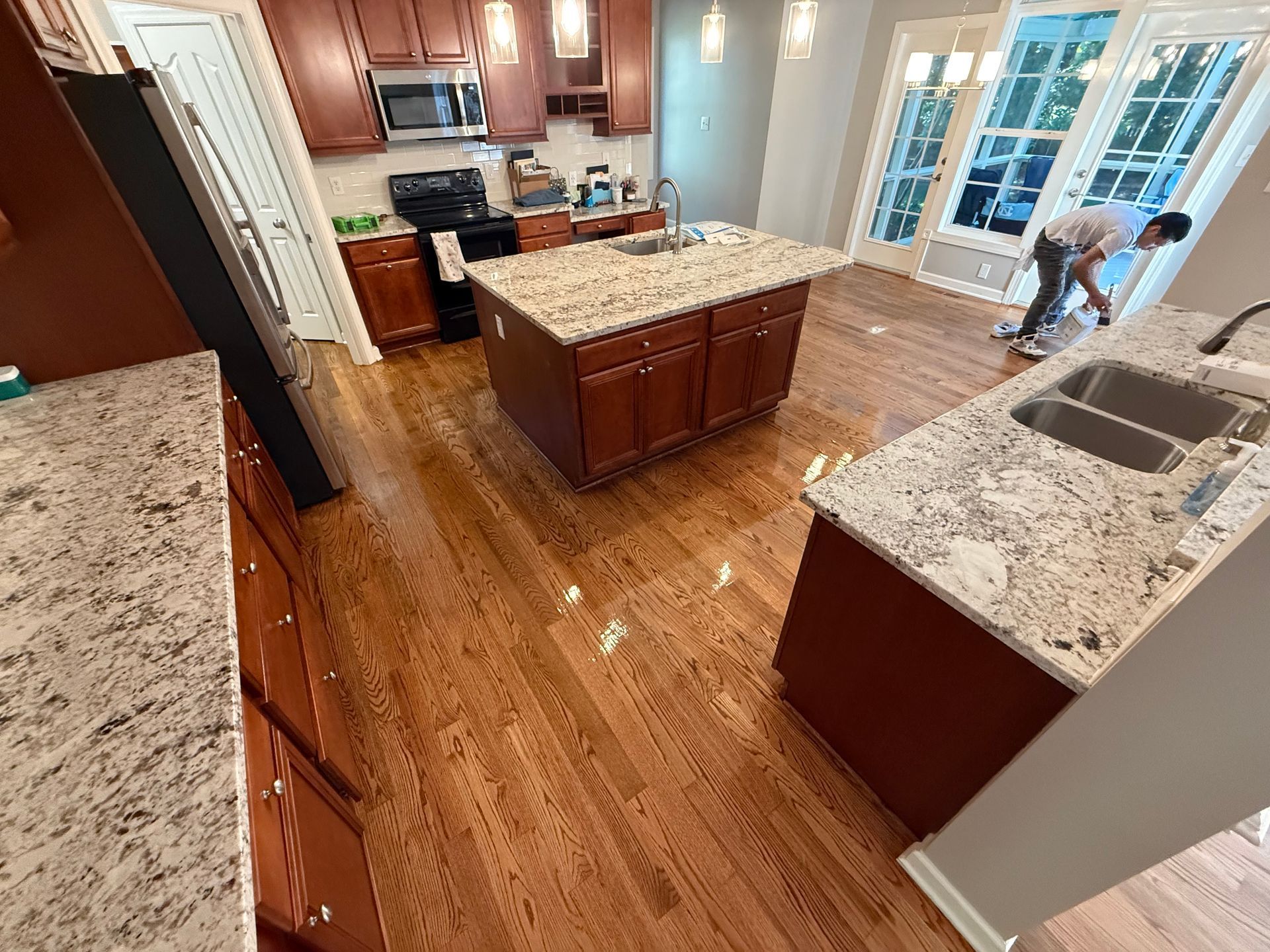 A man is cleaning a kitchen with granite countertops and hardwood floors.