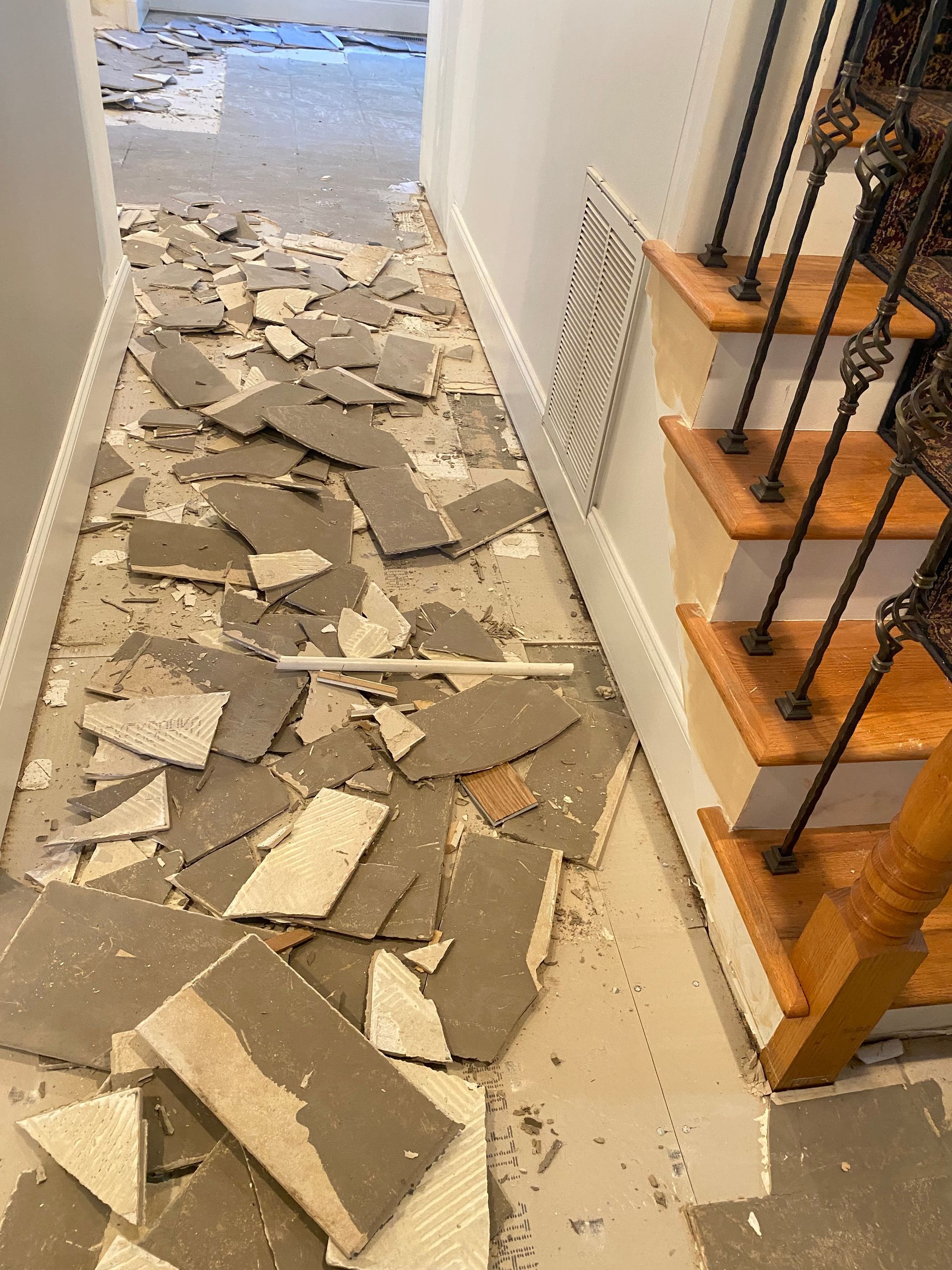 A hallway with stairs and a lot of broken tiles on the floor.
