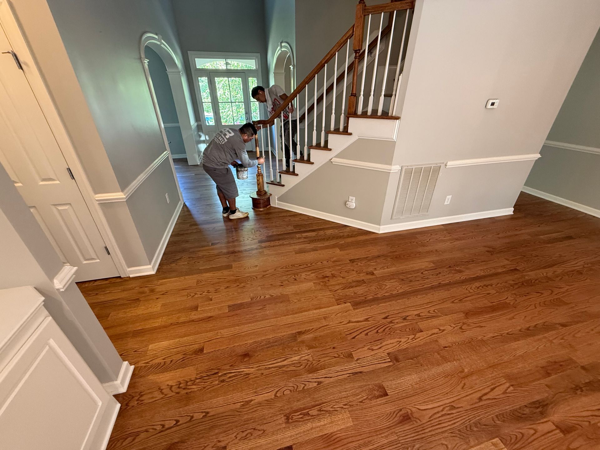 A man is standing on a wooden floor next to a staircase.