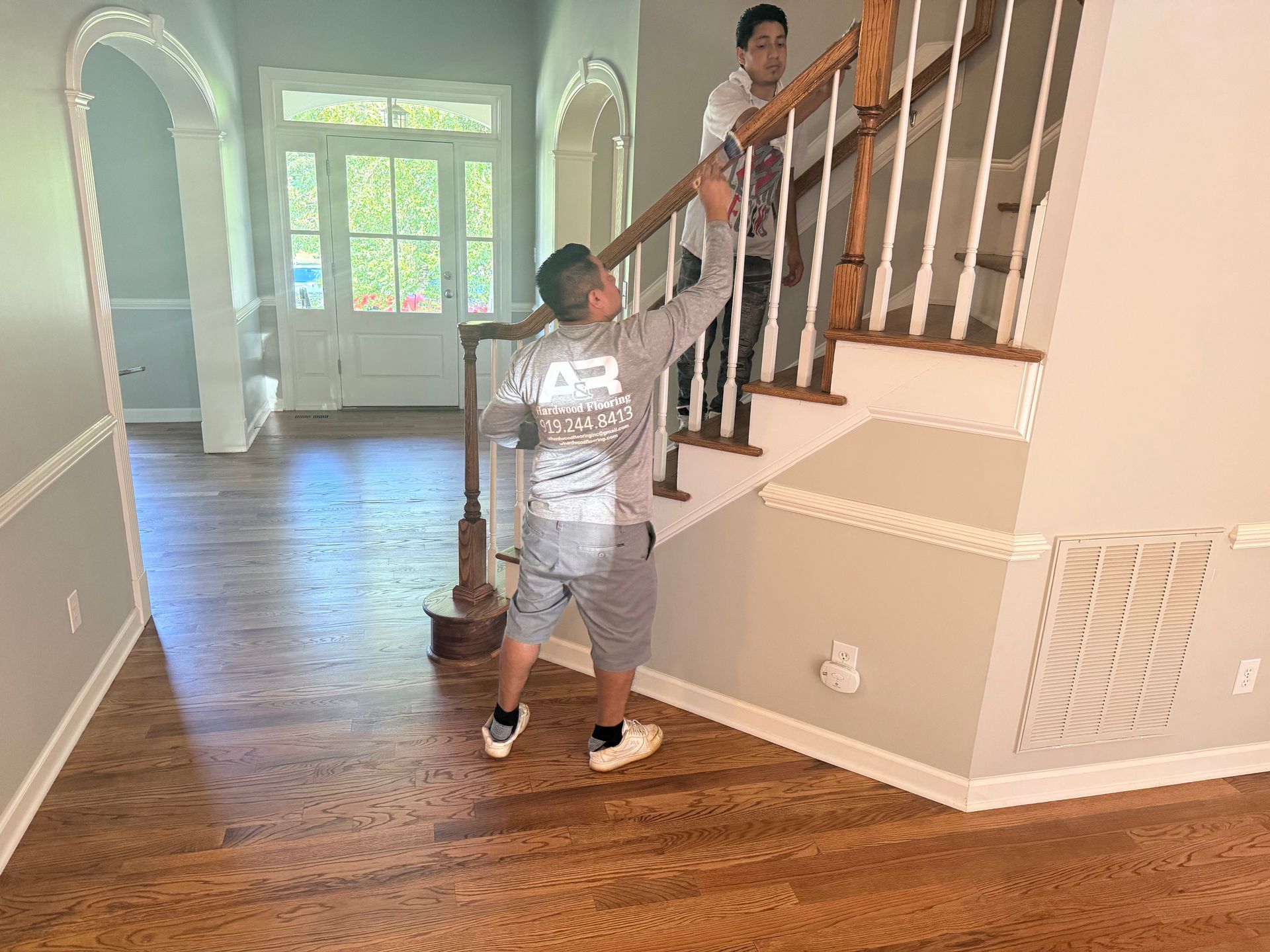 Two men are working on a stair handrail inside a house.