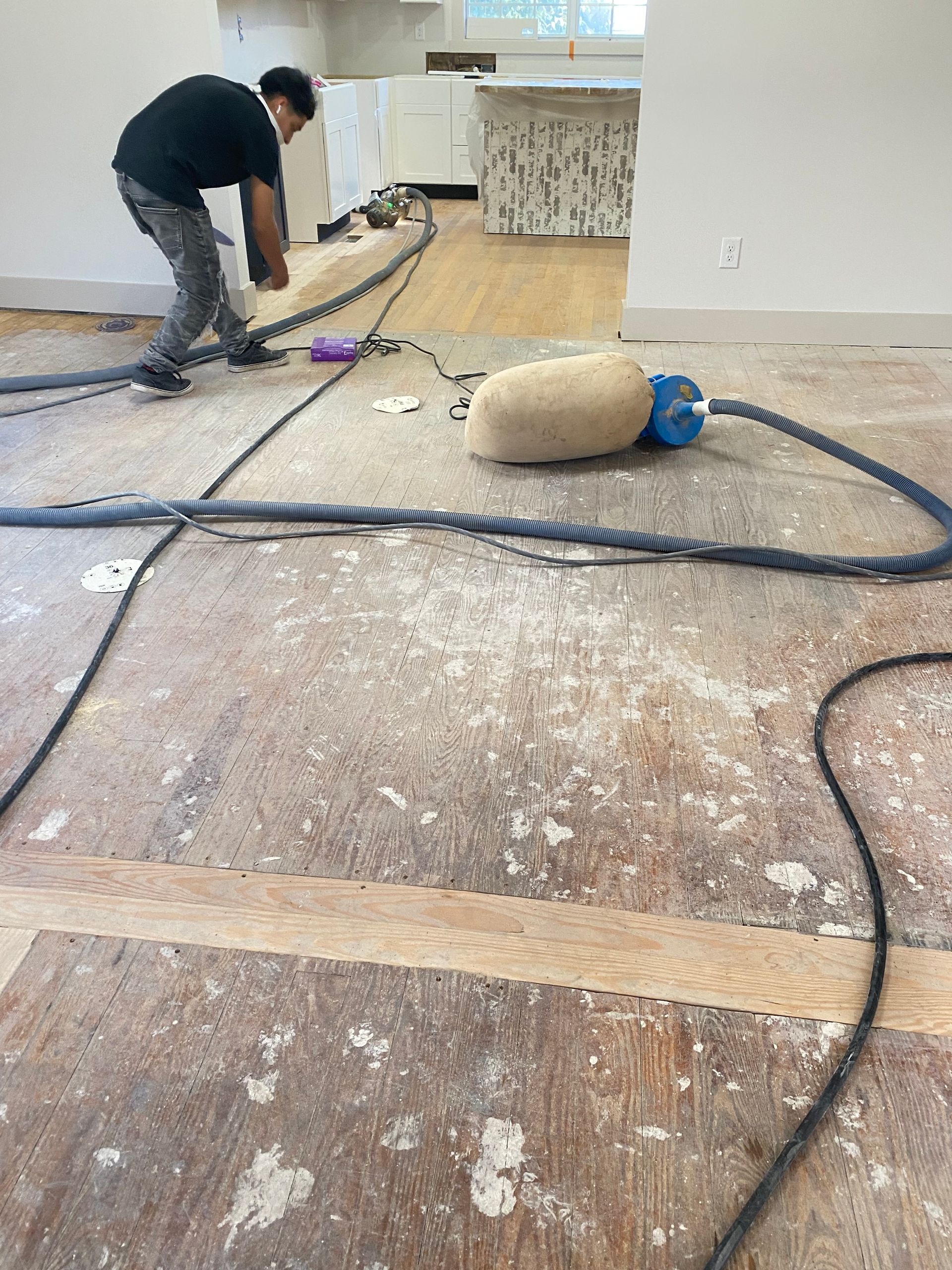 A man is working on a wooden floor with a vacuum cleaner.