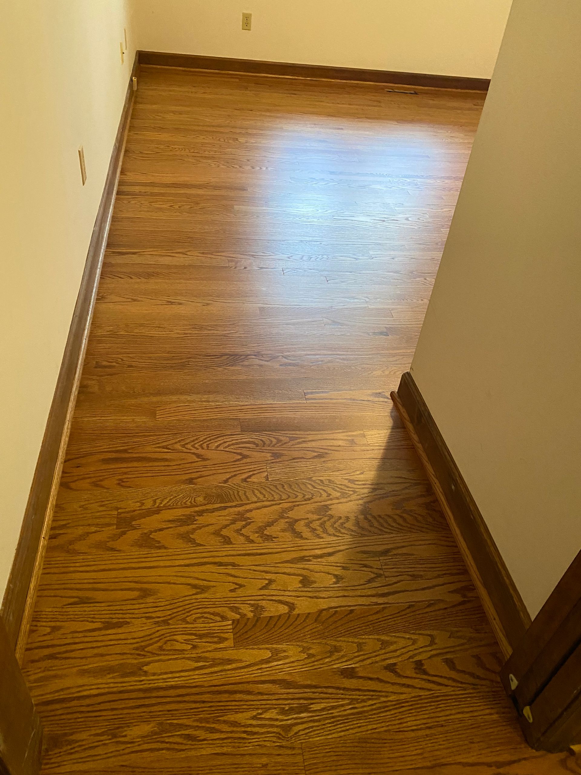 A hallway with hardwood floors and a white wall.