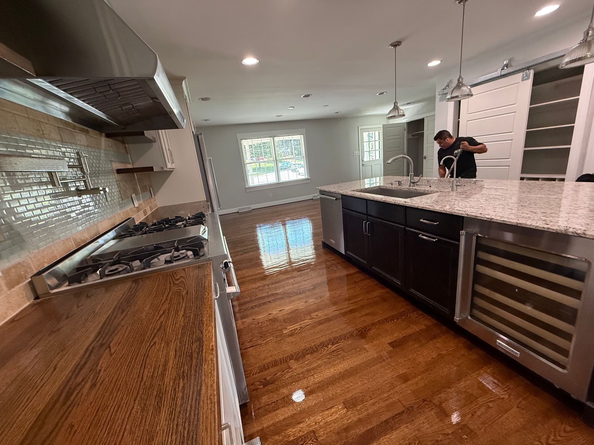 Modern kitchen with island, stainless appliances, wood floors, and a person.