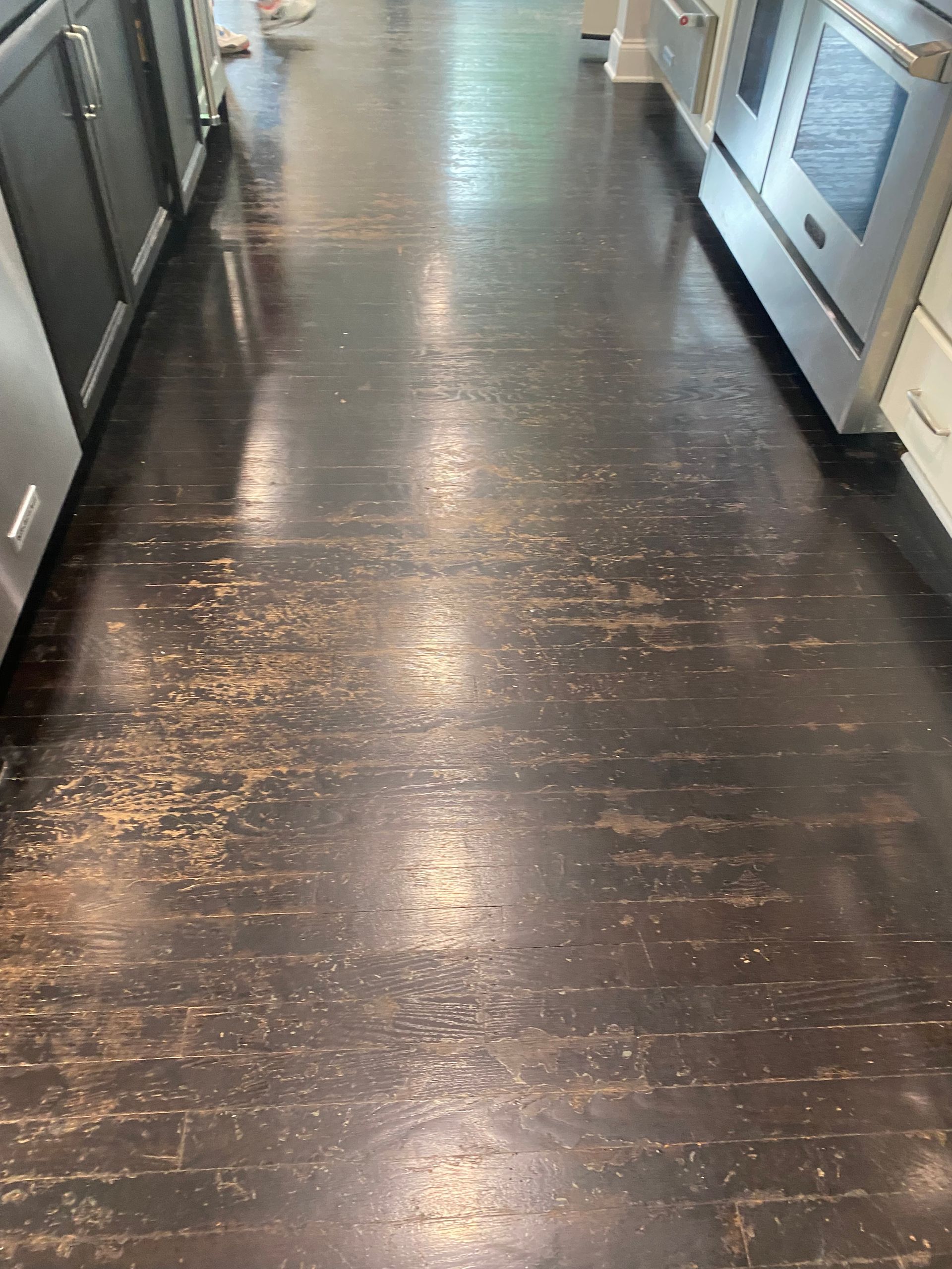 Dark brown hardwood floor with significant wear and visible light-colored damage, located in a kitchen.