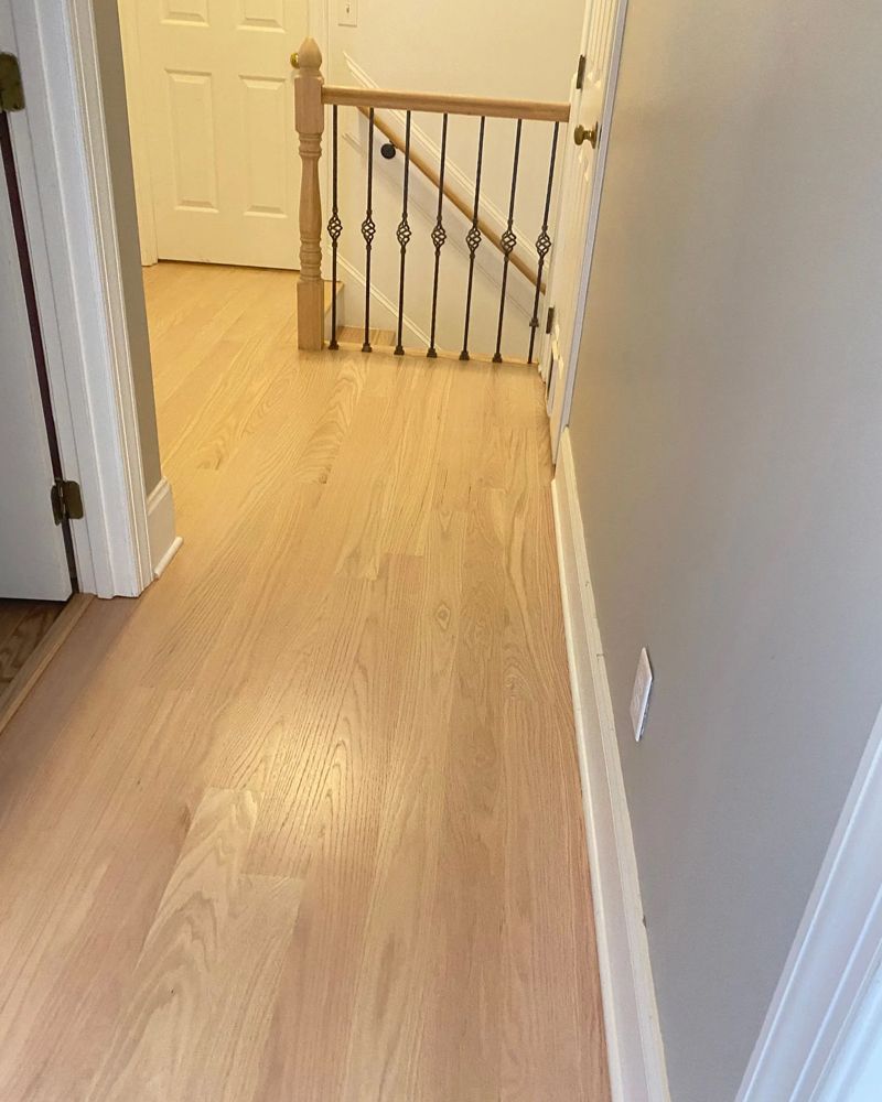 A hallway with hardwood floors and a staircase in the background.