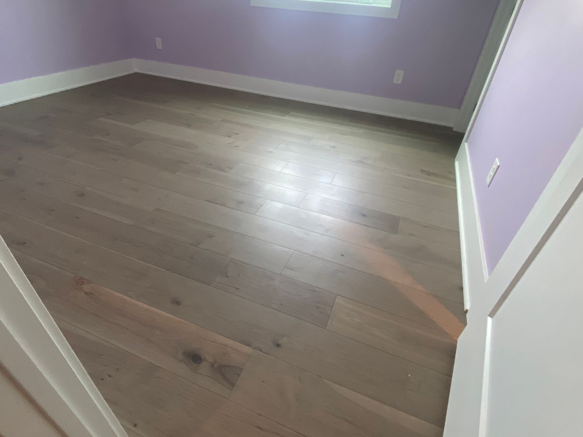 Empty room with light wood floors, lavender walls, and white trim, viewed from the doorway