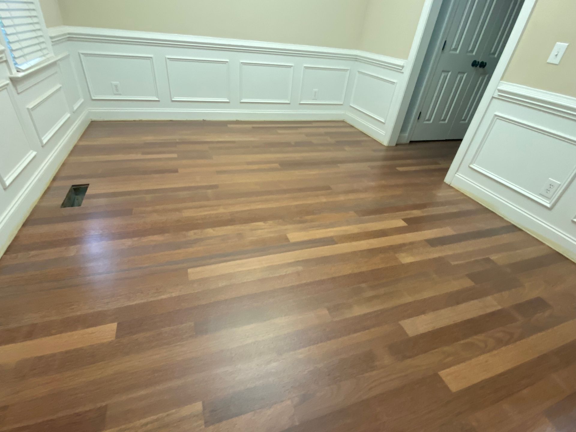 Empty room with wood floor, white paneled walls, and a gray door.