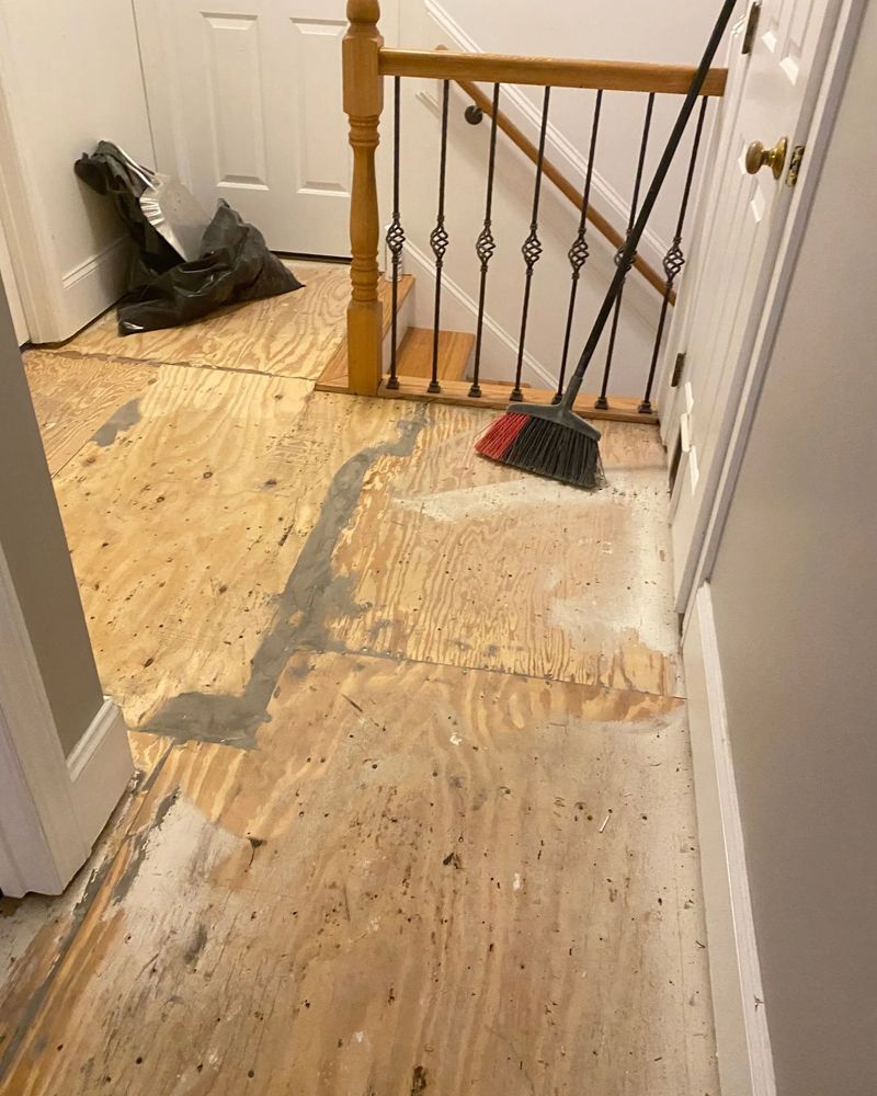 A broom is sitting on a wooden floor next to a staircase.