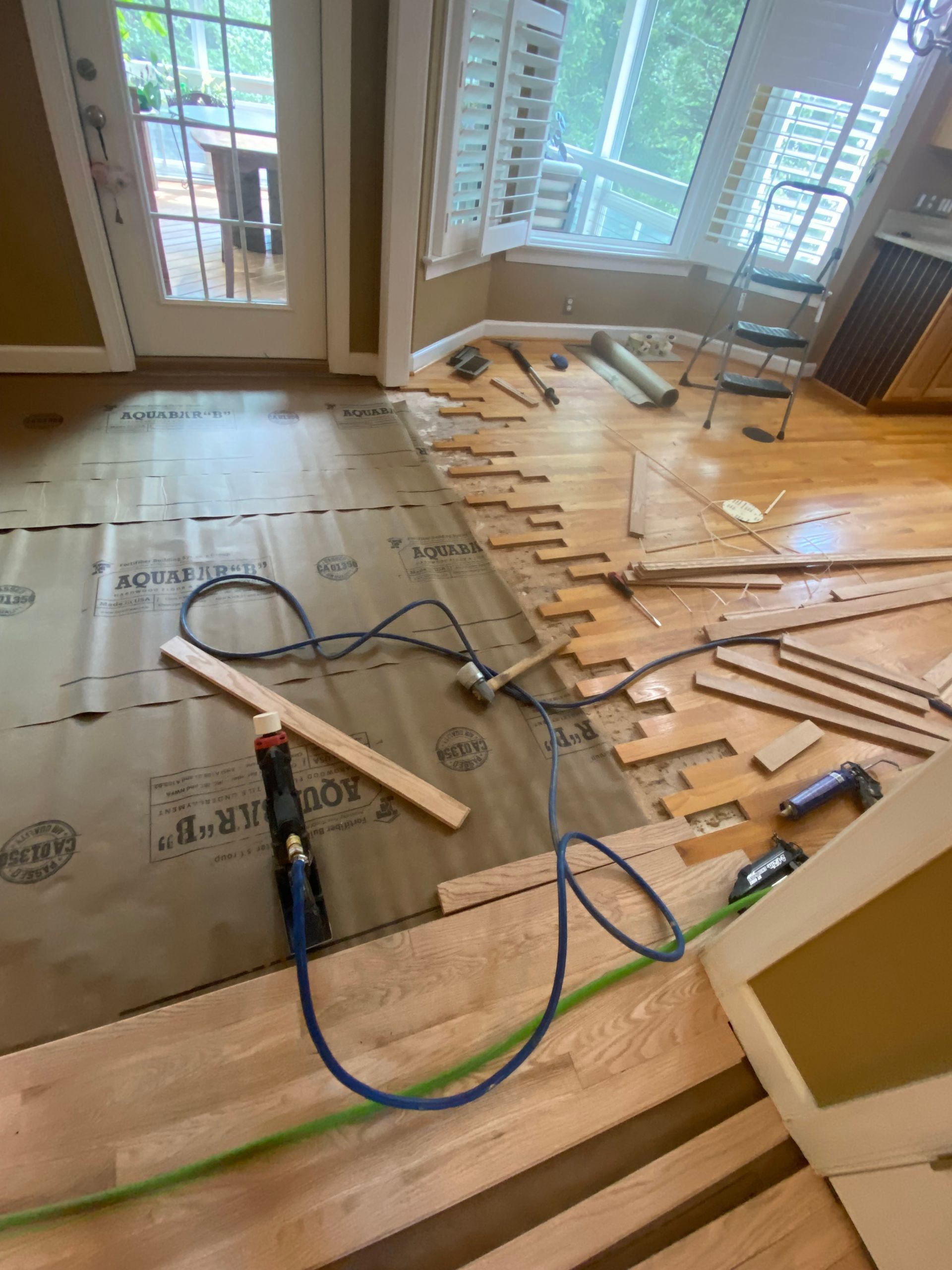 Renovated room with underlayment, loose floorboards, and tools on a wood floor near French doors