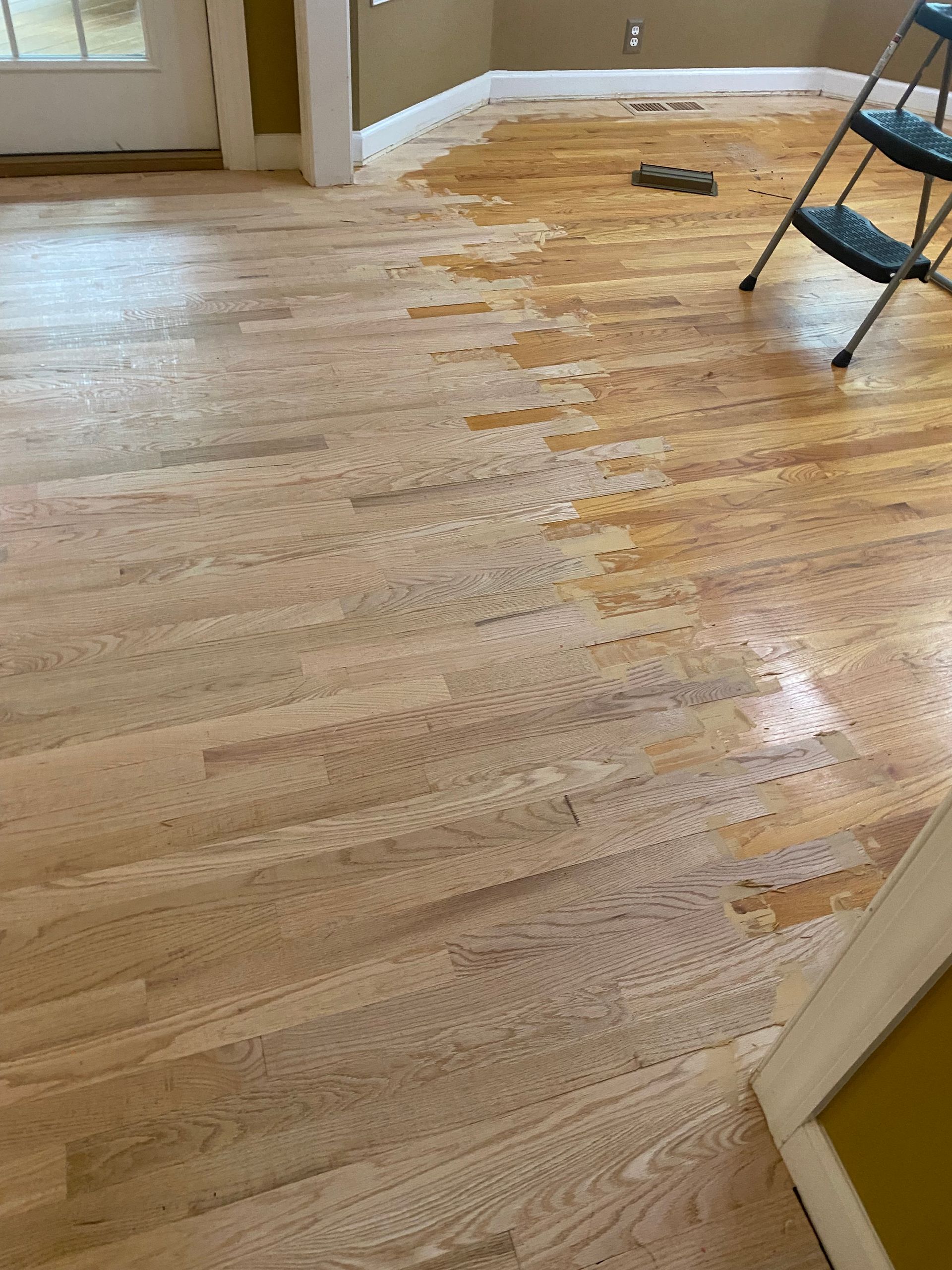 Water-damaged hardwood floor with peeling finish in an empty room, showing a chair and doorway.