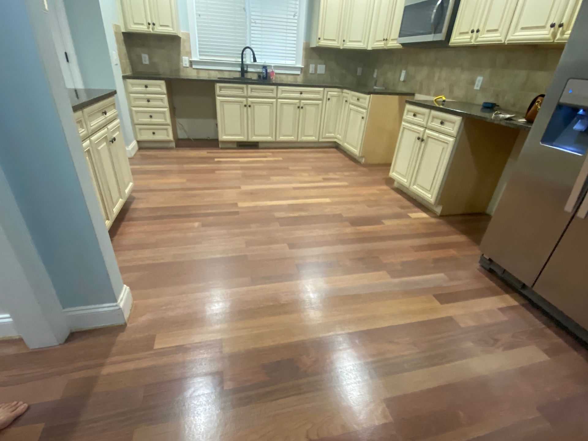Empty kitchen with cream cabinets, stainless steel appliances, and wood-look flooring.