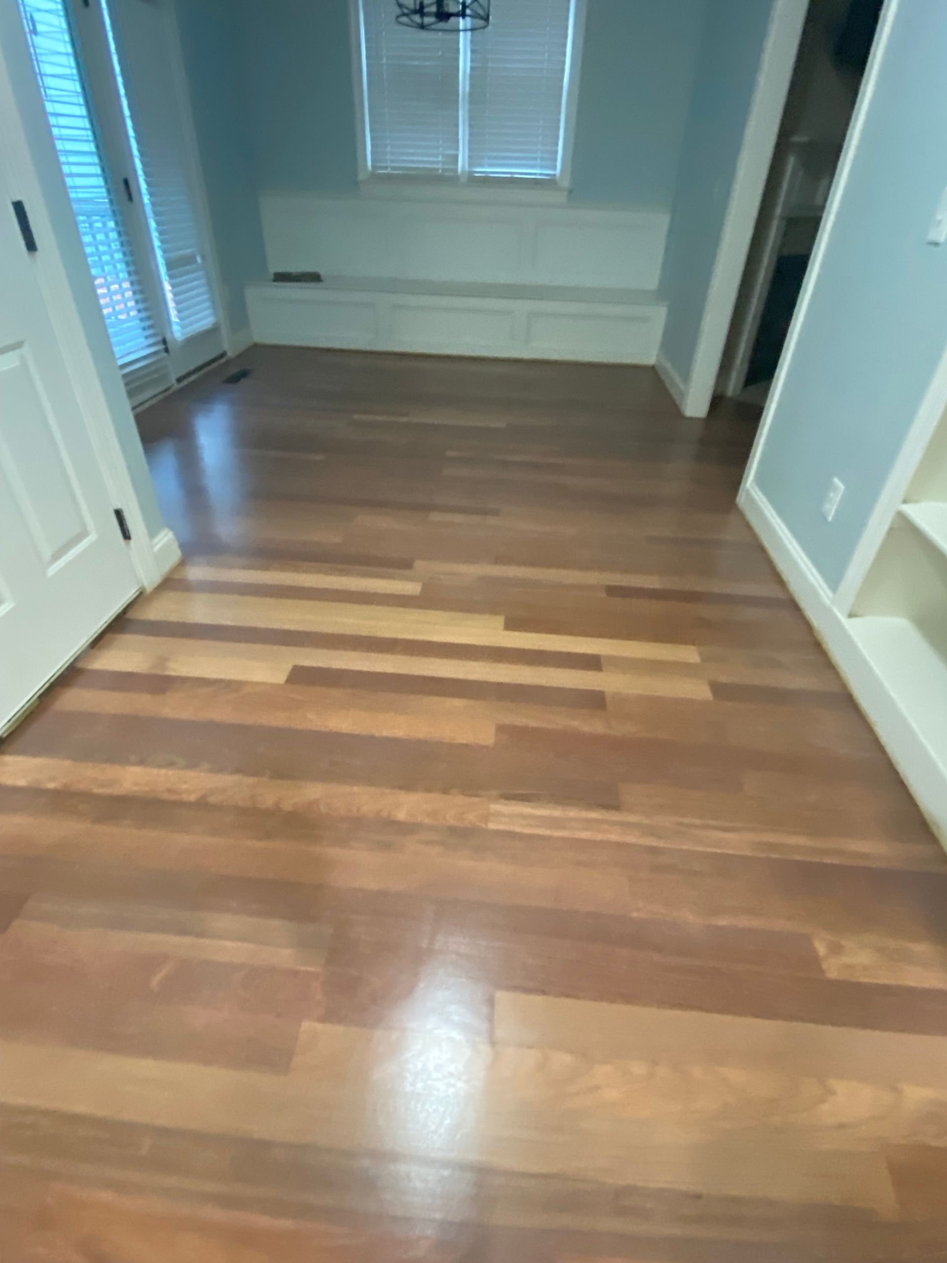 Wooden hallway with polished floors, white trim, and a window at the far end