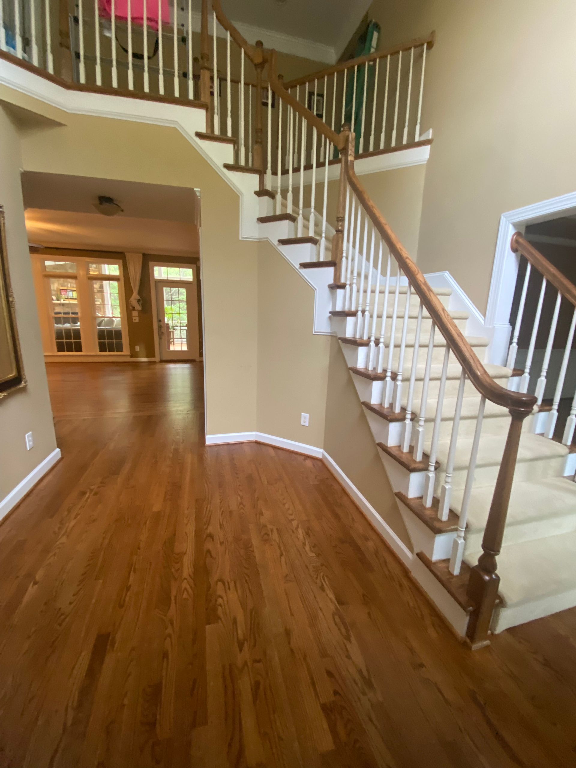 Spacious foyer with hardwood floors, staircase, and double front doors in a light-colored home