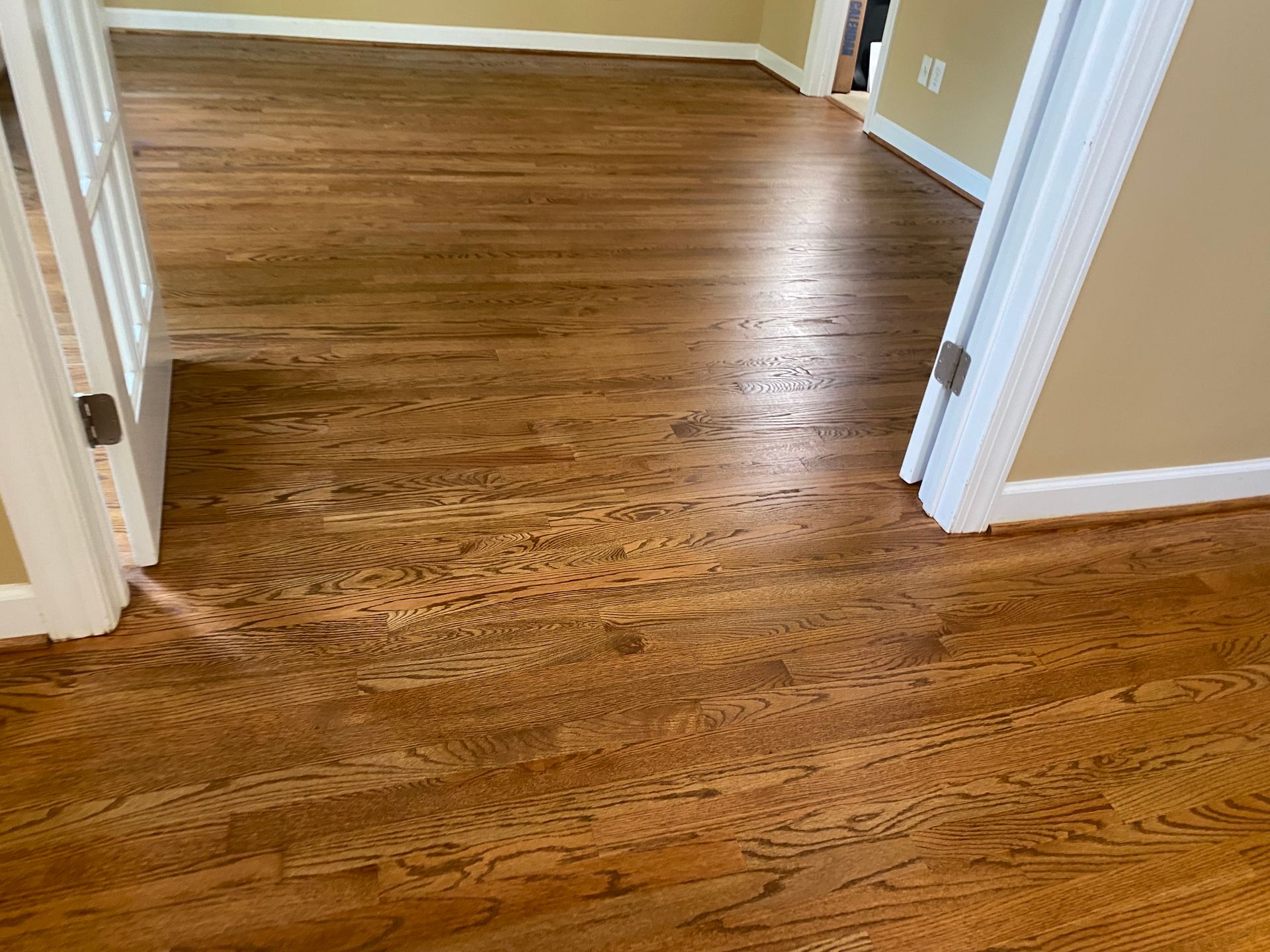 Empty room with polished hardwood floor and open doorways to beige walls.