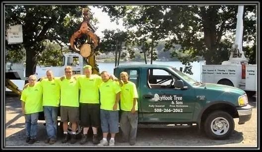 Skyhook Tree & Trim team posing beside a green truck in front of equipment and trees.