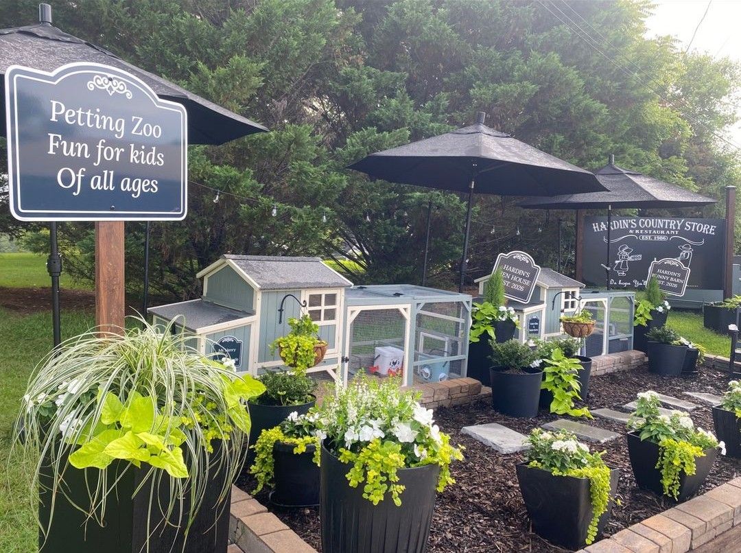 Garden display of pet items with black umbrellas and a chalkboard sign reading “Petting Zoo Furs for Kids of all ages”
