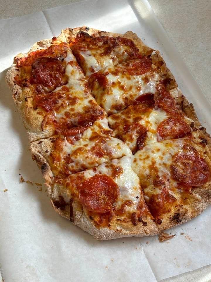 A pepperoni pizza is sitting on a piece of paper on a table.