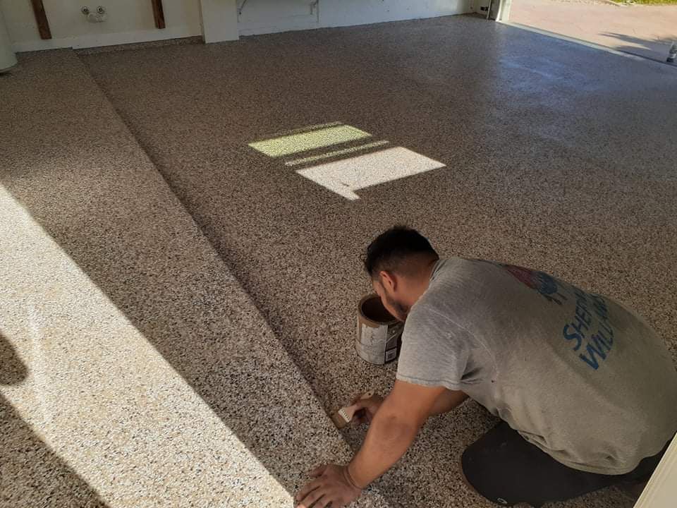 Man applying sealant to a speckled epoxy garage floor. The floor is tan, with light and dark speckles.