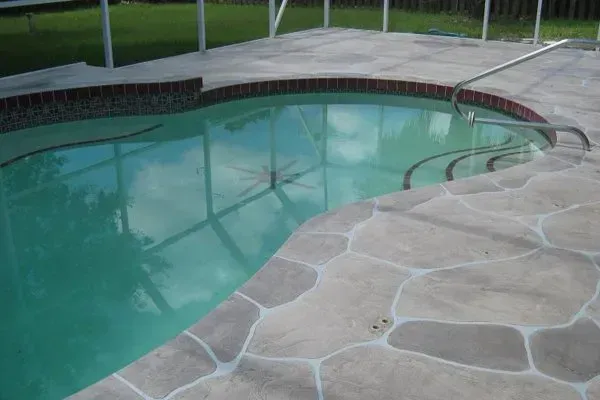 Swimming pool with steps and decorative stone edging; green water, bright outdoors.