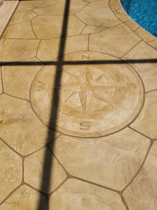 Stone patio with compass design, bordered by pool edge, shadow cast.