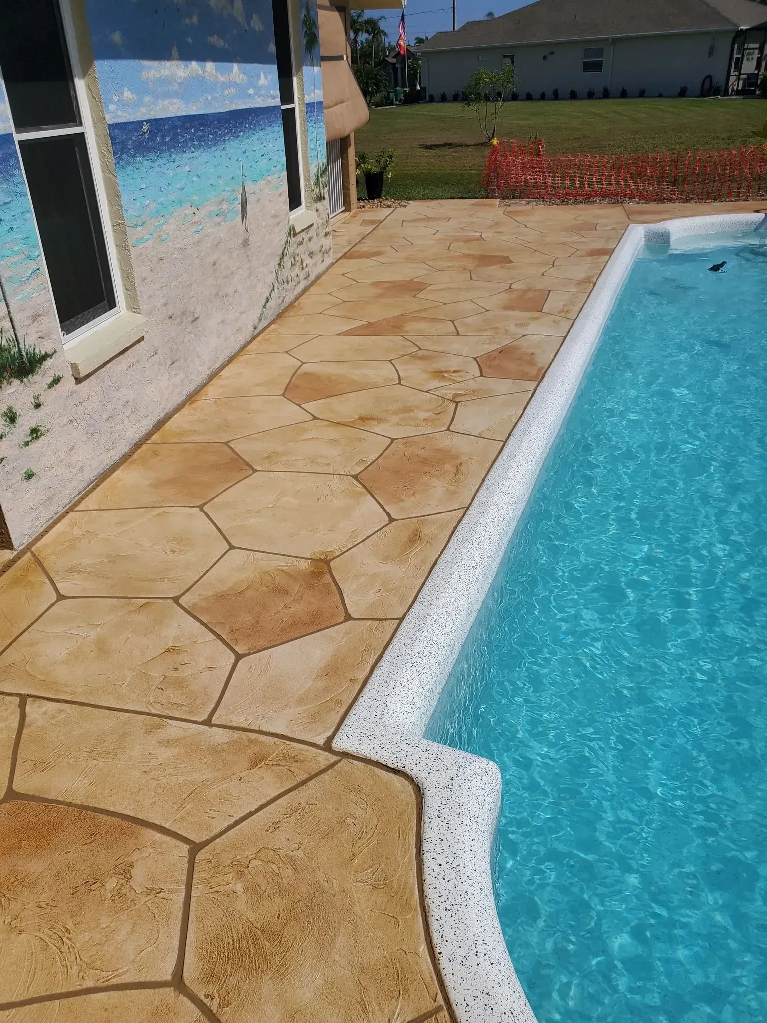 Concrete patio with hexagonal design next to a pool with turquoise water, near a painted wall.