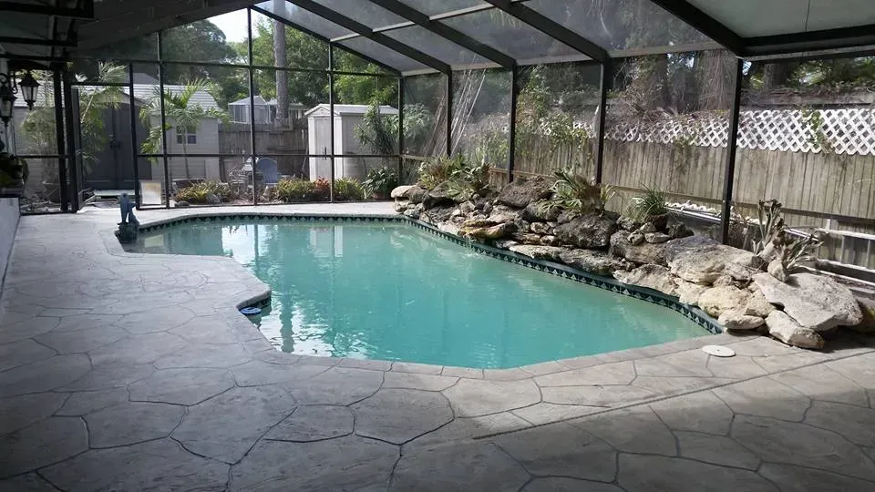 Pool area with turquoise water, rock features, and a screened enclosure.