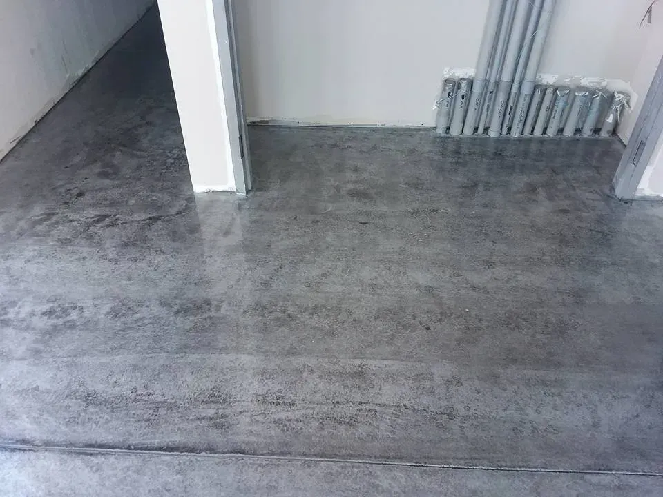 Concrete floor in a room, with a white doorway and conduits running along the wall.