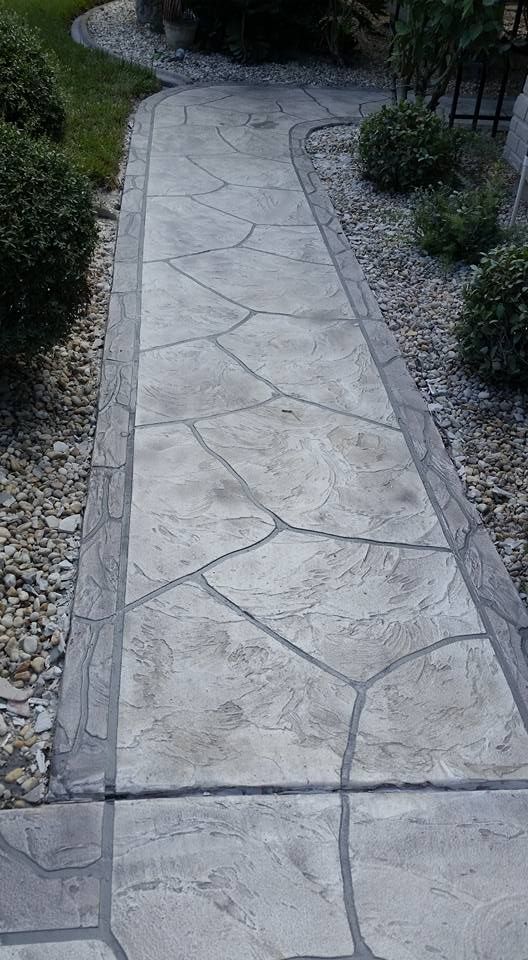 Stone pathway winding through a garden, bordered by stone and shrubs.
