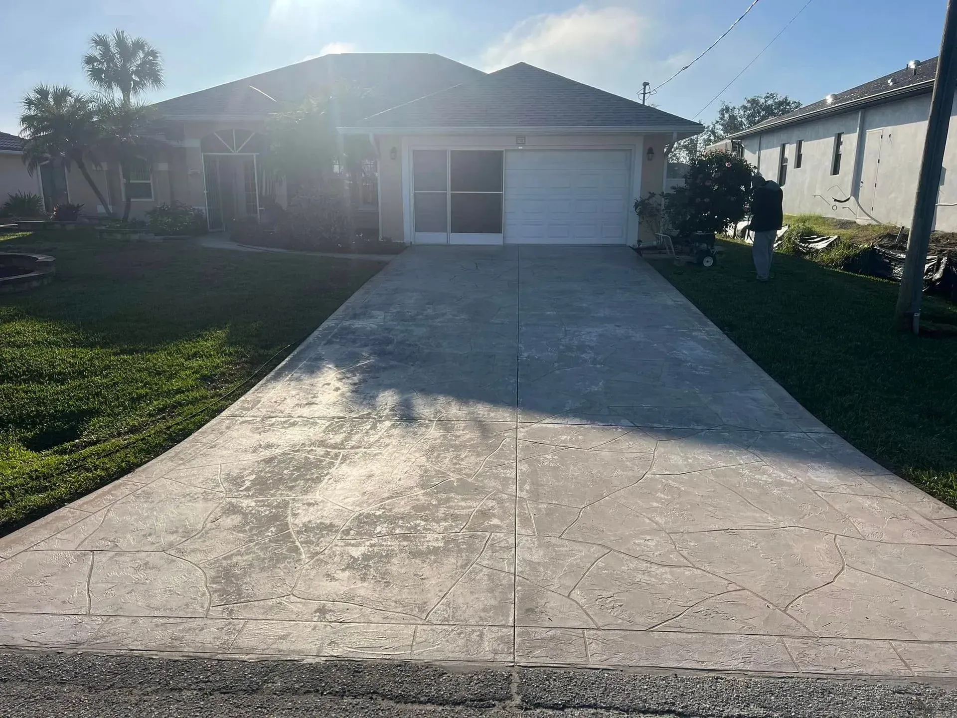 House with concrete driveway; green lawn, cloudy sky.