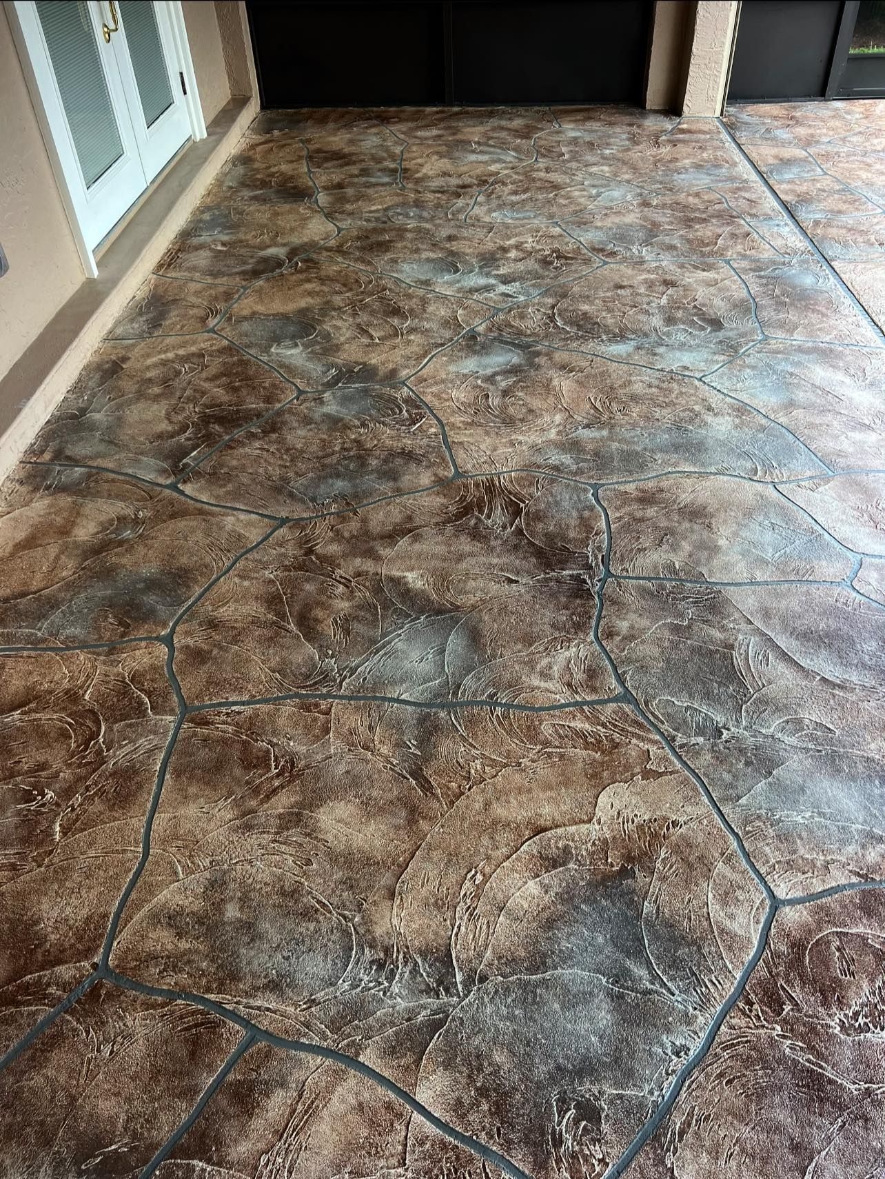 Brown and gray stamped concrete patio, resembling flagstones, in front of a house with a white door.