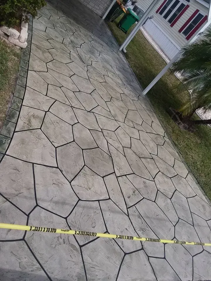 Gray concrete driveway with dark lines, textured with irregular shapes. Yellow caution tape across the bottom.