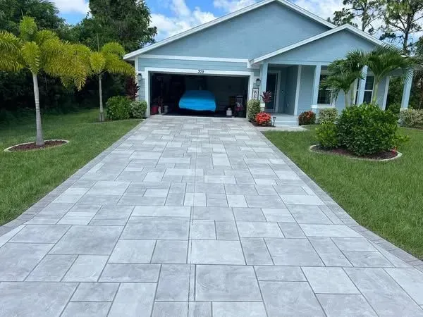 Paver driveway leading to a blue house with a garage; a car is inside.