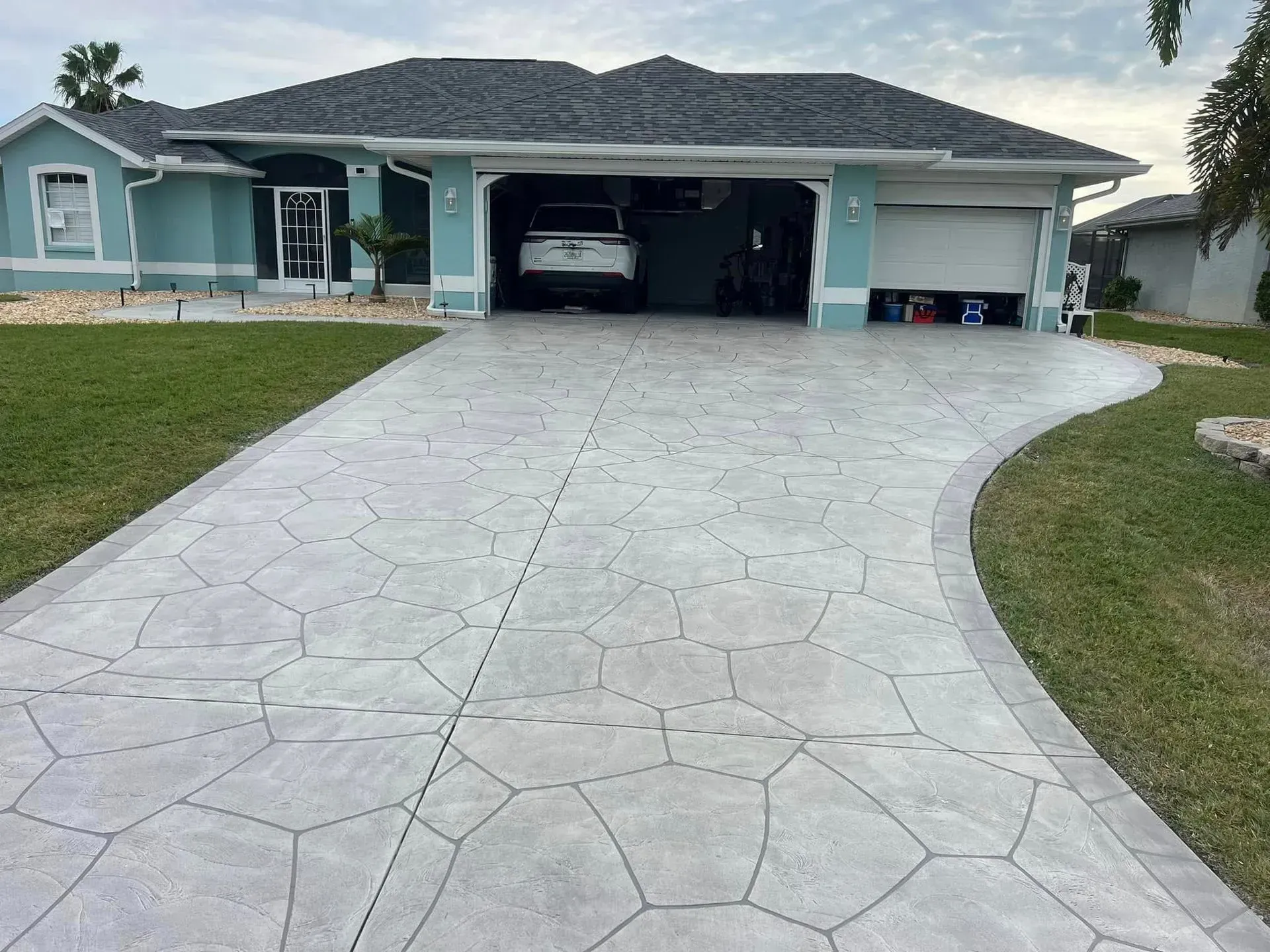 Light gray stamped concrete driveway leading to a teal house with open garage.