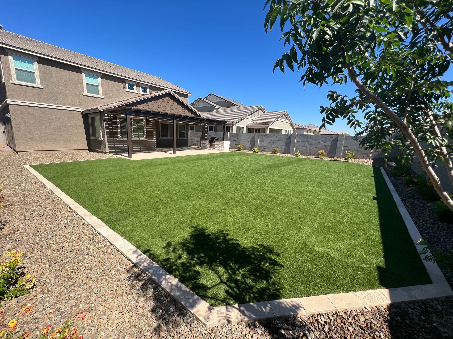 Backyard with artificial turf, patio, and gravel landscaping under a sunny sky.