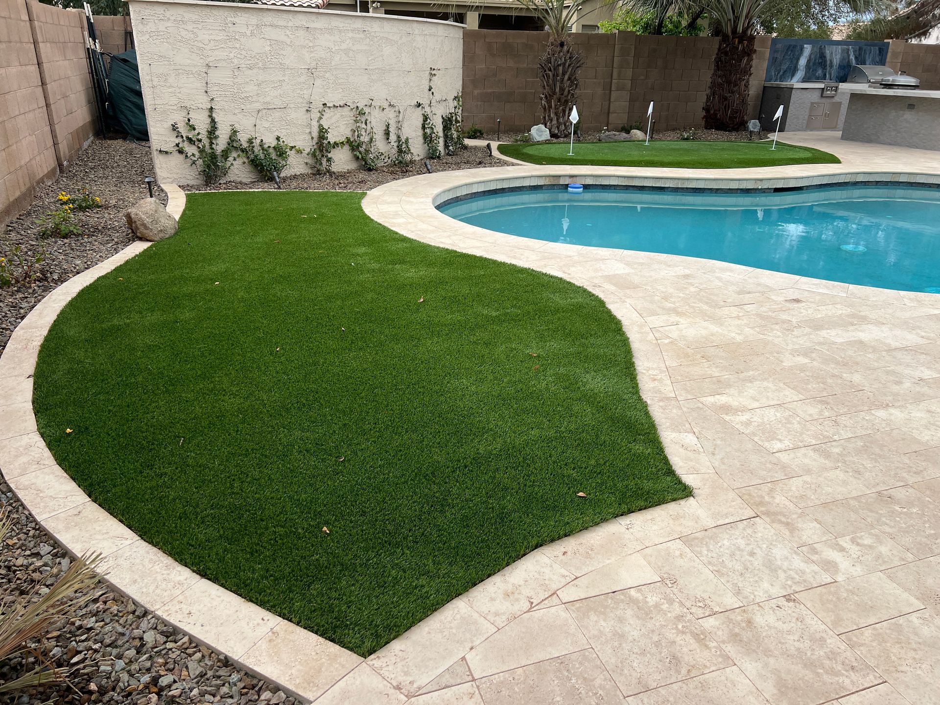 A backyard with a pool, green artificial grass, and stone patio.